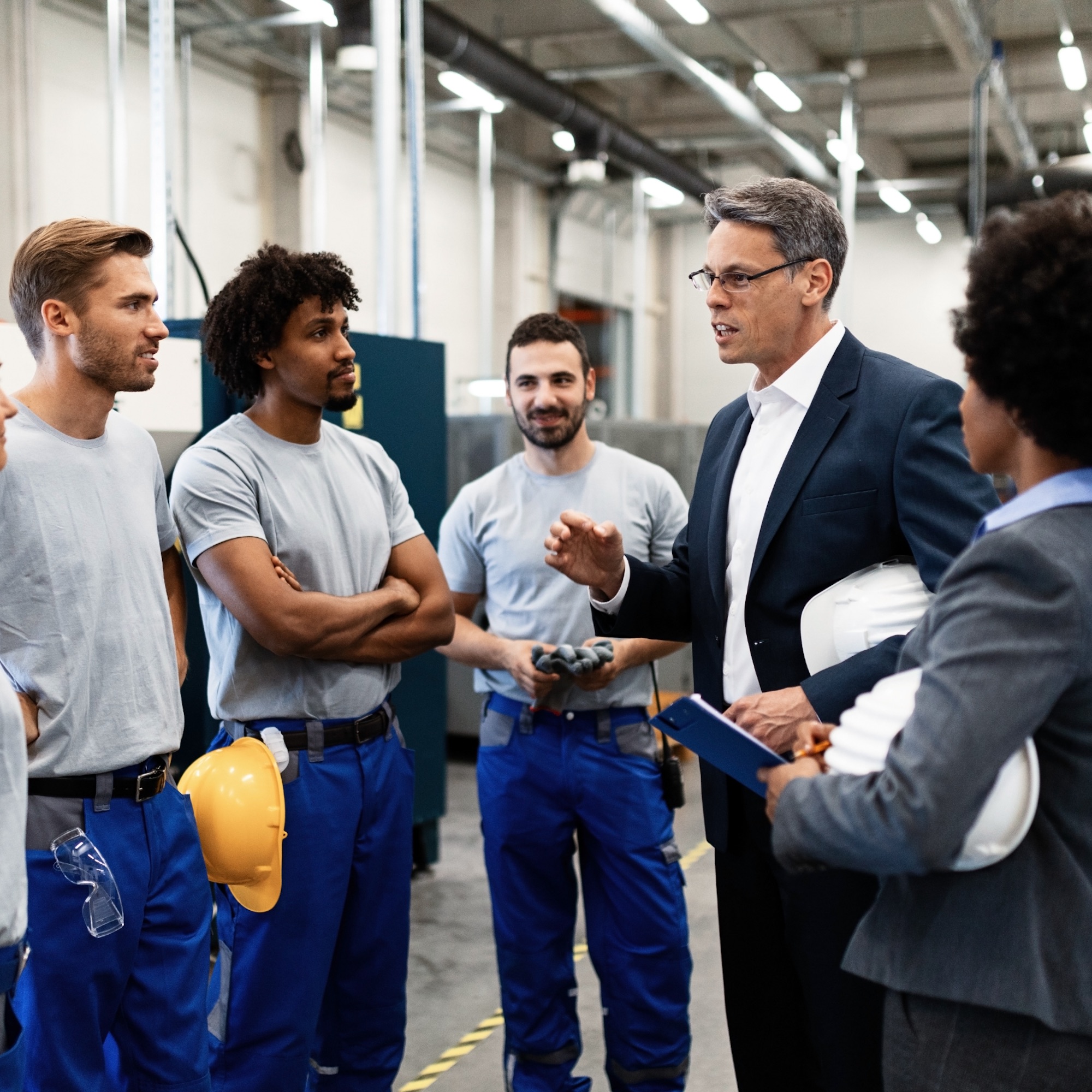 corporate-manager-talking-group-manual-workers-while-having-staff-meeting-factory@2x